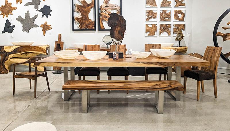 a natural wood dining table and chairs in front of a wall with free form wood art